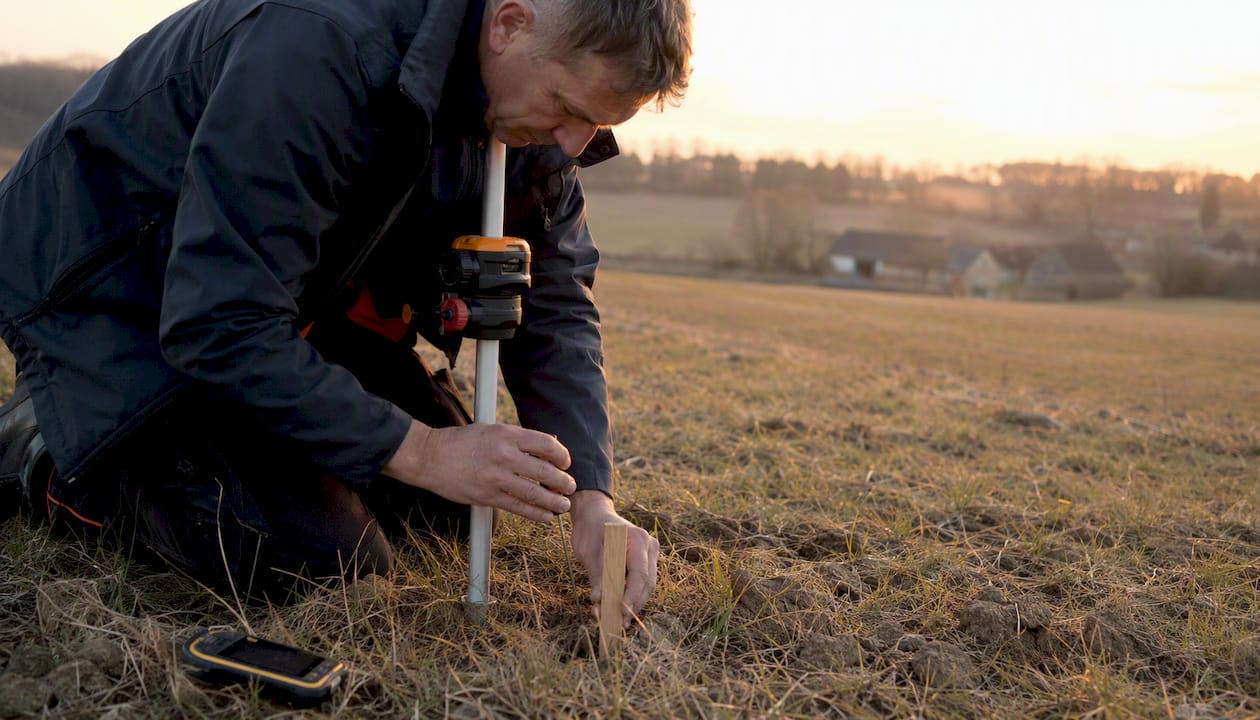 1786599415228_Surveyor-setting-land-boundary-stakes-outdoors Geodet v terénu vytyčuje hranice pozemku a umisťuje hraniční kolíky.